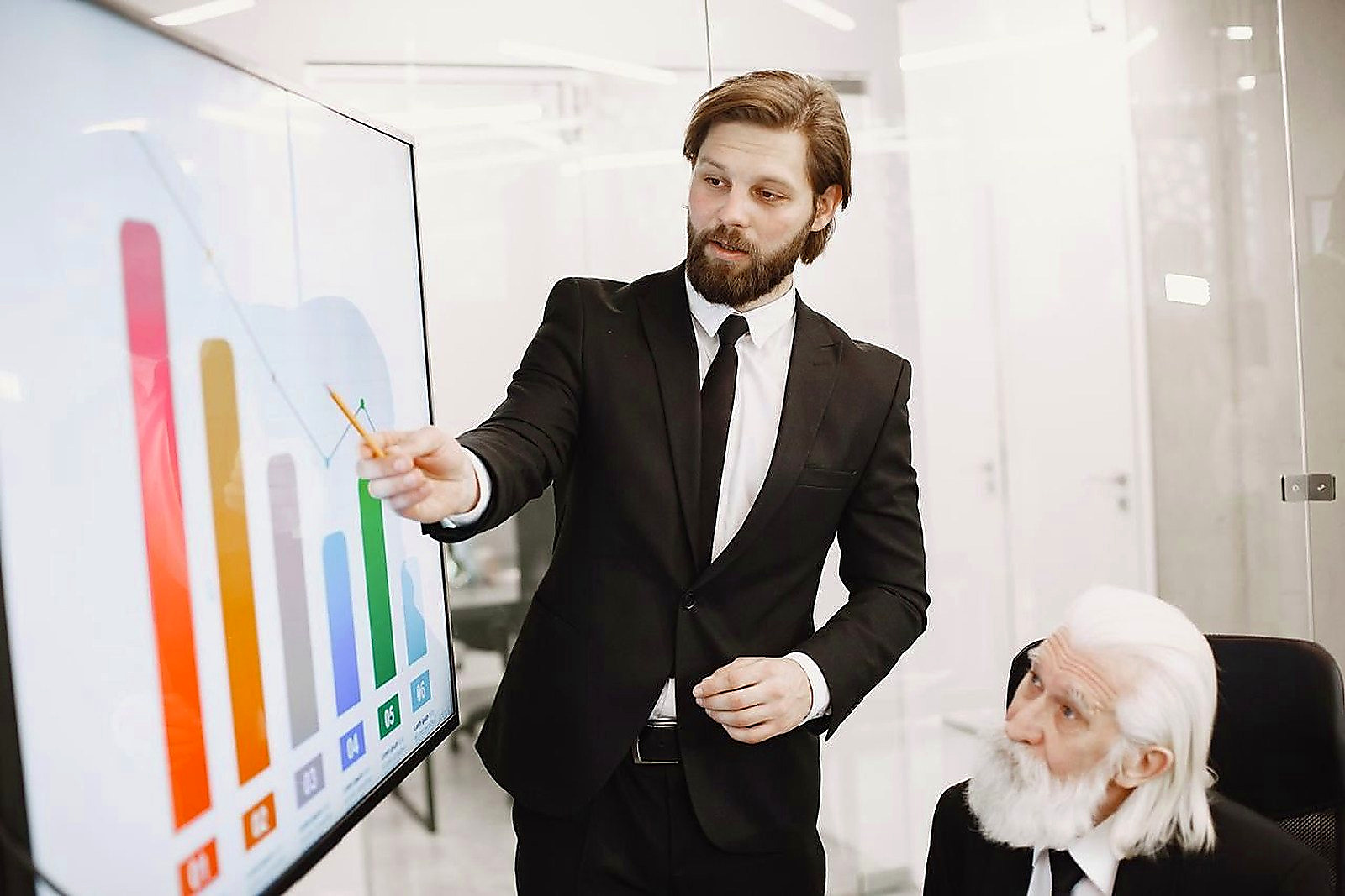 Free Two businessmen discussing data trends during a presentation in a modern office setting. Stock Photo